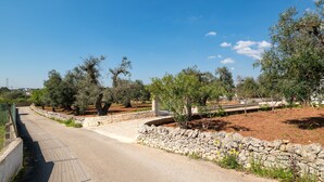 A paved road with stone walls and trees, leading to a building with a stone facade.