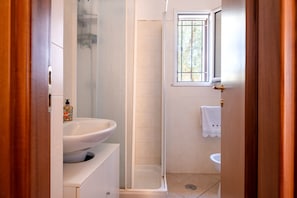 A bathroom with a shower, sink, and window.
