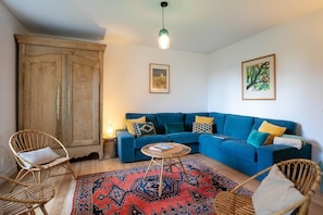 A living room with a blue sofa, wicker chairs, a patterned rug, and a wooden cabinet.