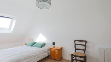 A bedroom with a bed, a nightstand with a lamp, a chair, a window, and a radiator.