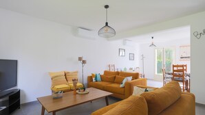 Ein Wohnzimmer mit Sofa, Couchtisch, Fernseher und einem Essbereich mit Stühlen und Tisch.