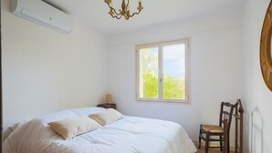 Ein Schlafzimmer mit Bett, Fenster, Sessel und Wandklimaanlage.