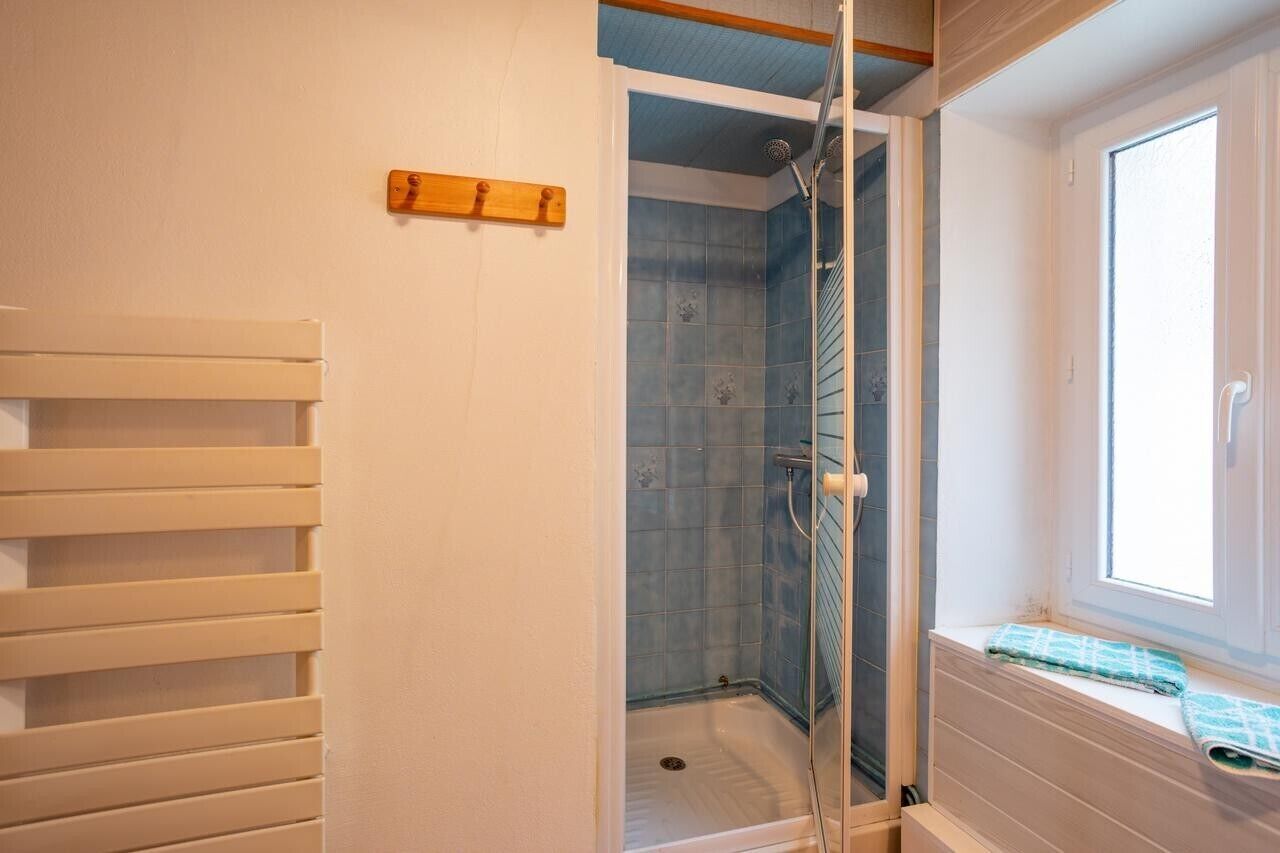 Een douche met een glazen deur, een raam met uitzicht en een houten bank.