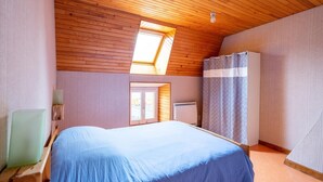 A bedroom with a wooden ceiling, a skylight, a bed, a wardrobe, and a radiator.