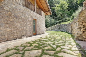 Un edificio de piedra con un balcón de madera, una pared de piedra y un área pavimentada con césped.