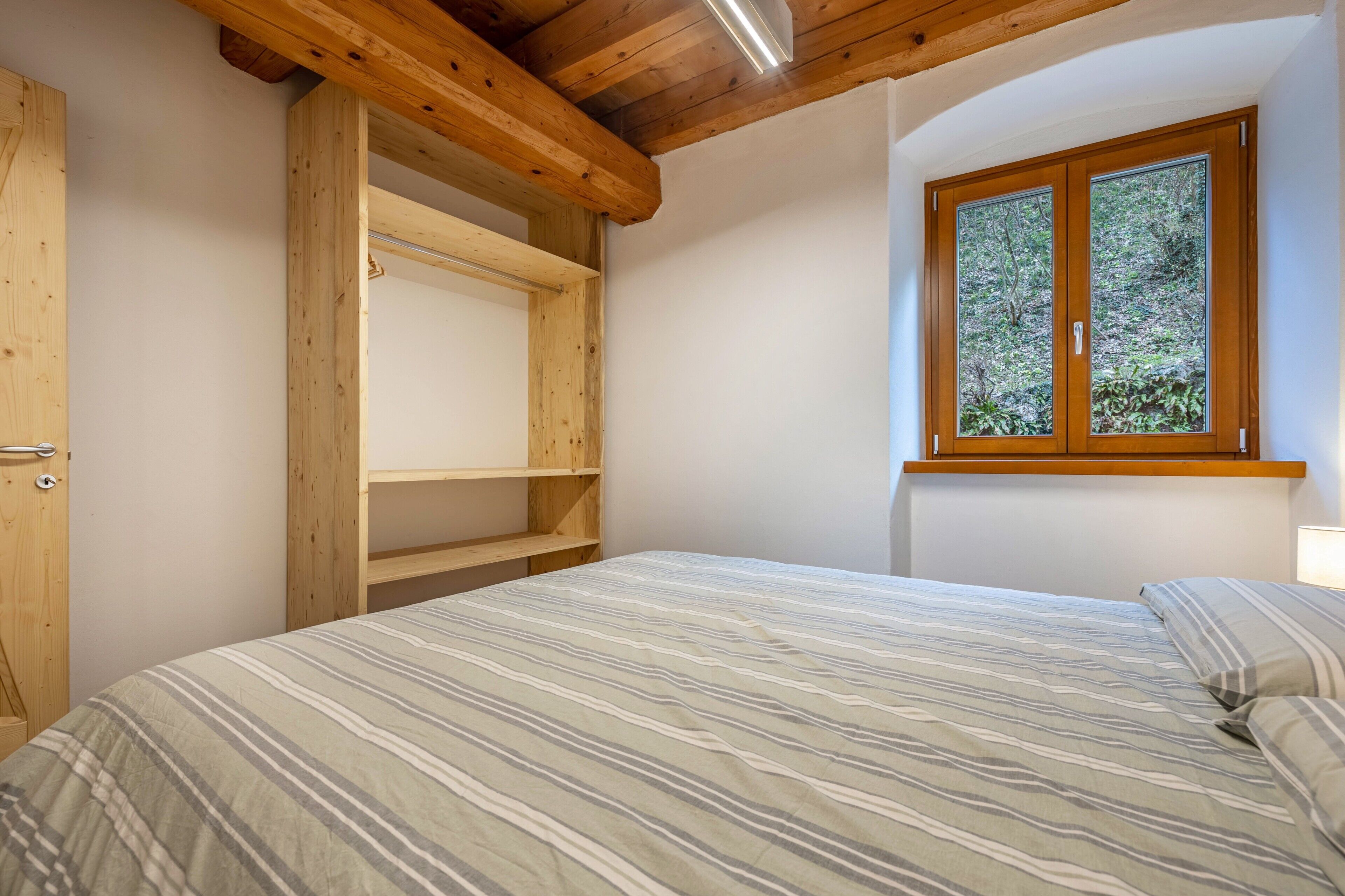Un dormitorio con cama, armario de madera y ventana con vistas a árboles.