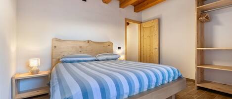 A bedroom with a wooden bed, a nightstand with a lamp, a wardrobe, and a wooden ceiling.