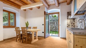 Een houten eettafel met stoelen, een keuken met een stenen muur en een houten plafond.