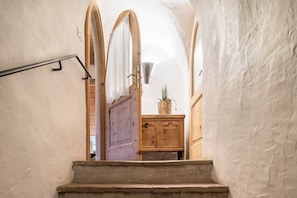 Uma escadaria leva a um quarto com uma porta de madeira, um armário pequeno e um vaso de planta.