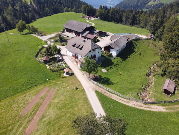A large, multi-story building with a sloped roof, surrounded by green fields and trees.