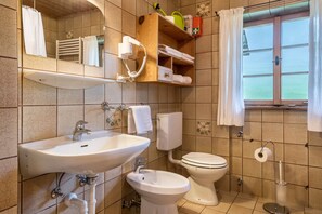 A bathroom with a sink, bidet, toilet, and a window with curtains.