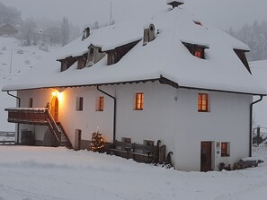 A snow-covered building with a staircase leading to a balcony, a small Christmas tree, and multiple windows.