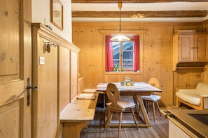 A wooden interior with a dining table, chairs, a window with red curtains, and wooden cabinets.