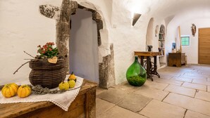 Un interior rústico con un arco de piedra, una mesa de madera con una cesta de flores y una botella verde.