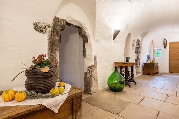 A rustic interior with a stone archway, a wooden table with a basket of flowers, and a green bottle.