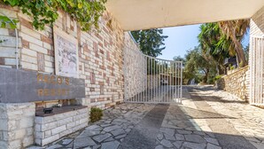 Un chemin de pierres mène à une entrée fermée par un portail sur lequel on peut lire : « PACO’S RESORT ».