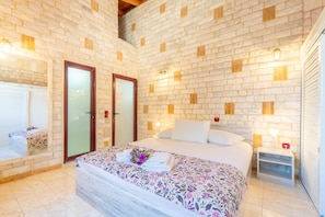A bedroom with a brick wall, a bed with floral bedding, a nightstand, and a small table with a lamp. - Country House 'Paco's Resort  Luxury Villa 31' with Sea View, Wi-Fi and Air Conditioning (Paxoi)
