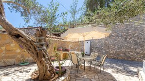 Eine Terrassenanlage im Freien mit Steinboden, einem Tisch mit Stühlen, einem großen Sonnenschirm und einem Baum.