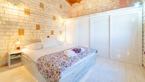 Ein Schlafzimmer mit Ziegelwand, einem Bett mit blumigem Überwurf, einem Nachttisch mit Lampe und einem Fenster mit Jalousien.