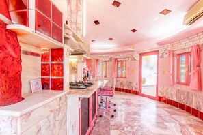 Een kamer in roze kleurstelling met een marmeren vloer, een kitchenette en een zithoek met een roze stoel.