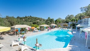 Piscina con sillas de descanso y sombrillas, rodeada de vegetación y un paisaje montañoso.