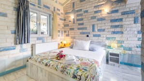 A bedroom with a bed, a window with curtains, a nightstand with a lamp, and a wall with a stone pattern. - Studio Apartment 'Paco's Resort Standard  4' with Mountain View, Wi-Fi and Air Conditioning (Paxoi)