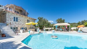 A swimming pool with lounge chairs and umbrellas, a stone building with a balcony, and a clear blue sky. - Studio Apartment 'Paco's Resort Standard  4' with Mountain View, Wi-Fi and Air Conditioning (Paxoi)