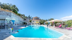 A swimming pool with a unicorn float, outdoor seating, and a stone building in the background. - Studio Apartment 'Paco's Resort Standard  1' with Mountain View, Wi-Fi and Air Conditioning (Paxoi)