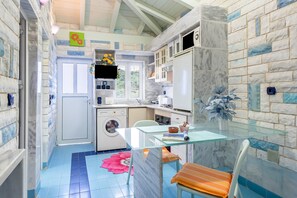 A compact kitchen with a washing machine, a glass table, and a chair with a cushion.