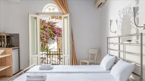 A hotel room with a bed, a desk, a chair, and a balcony with flowers. - Studio Apartment 'En Tino 1' with Balcony, Wi-Fi and Air Conditioning (Tinos)
