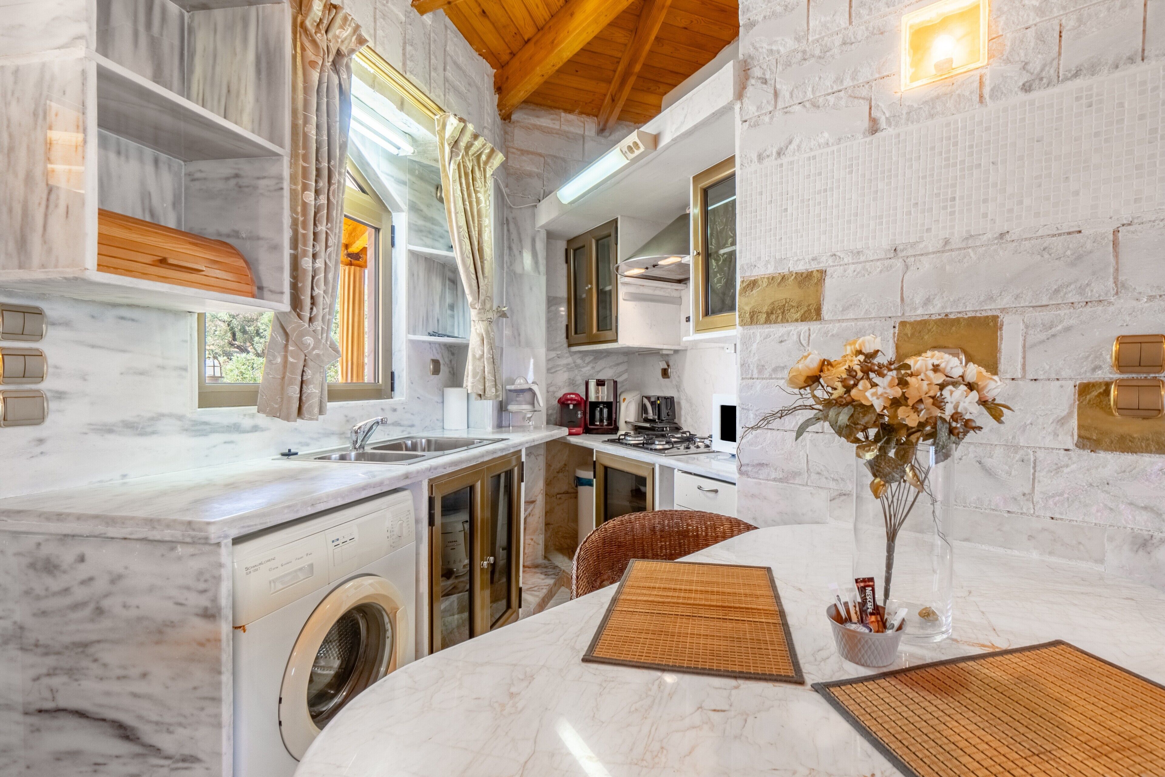 A compact kitchen with a washing machine, a dining area with a table, and a vase with flowers.