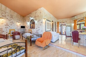 Habitación de hotel con pared de ladrillo, cama, sillón, sofá, televisor y zona de comedor.