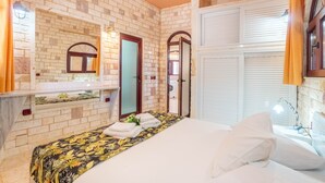 Ein Hotelzimmer mit Backsteinwand, einem Bett mit Blumenmuster-Überwurf, einem Spiegel und einem Fenster mit Vorhängen.