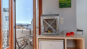 A compact kitchenette with a refrigerator, a small oven, and a window with a view of buildings. - Studio Apartment 'En Tino 3' with Balcony, Wi-Fi and Air Conditioning (Tinos)