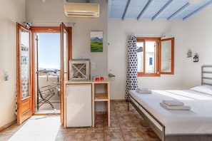 A bedroom with a bed, a desk with a computer, a small refrigerator, and a window with a view.