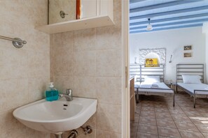 Une salle de bain avec un lavabo, un miroir et un porte-serviettes. Une chambre avec deux lits et une fenêtre.