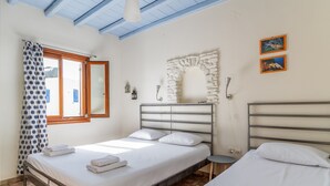 A bedroom with a bed, a small table, a stone archway, and a window with curtains. - Studio Apartment 'En Tino 3' with Balcony, Wi-Fi and Air Conditioning (Tinos)