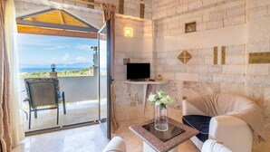 Habitación con pared de piedra, televisor, mesa de vidrio, una silla y vista al mar.