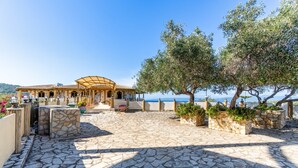Eine terrasse mit Steinpflaster, Sitzgelegenheiten im Freien, einer Pergola und Olivenbäumen.