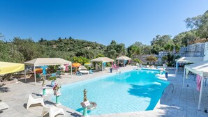 Ein Swimmingpool mit Liegestühlen und Sonnenschirmen, umgeben von Grünflächen und Steinmauern.