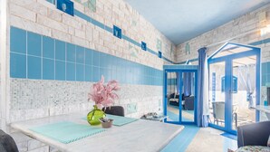 Een kamer met een betegelde muur, een tafel met een vaas en uitzicht door een geopende deur.