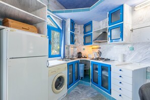 Een kleine keuken met blauwe kastjes, een wasmachine en een spoelbak.