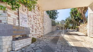Un chemin de pierre mène à une entrée fermée par un portail, sur lequel on peut lire l’inscription « PACO’S RESORT ».