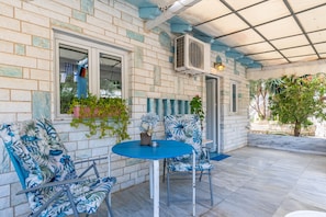 Un patio cubierto con una mesa y sillas, una planta en maceta y una ventana con cortinas.