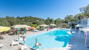 Une piscine entourée de verdure et de murs en pierre, avec des chaises longues et des parasols.