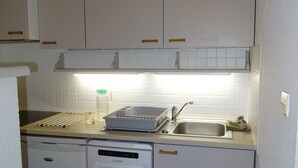 Une cuisine compacte avec des meubles blancs, un lave-vaisselle et un plan de travail muni d’un égouttoir et d’un support à vaisselle.