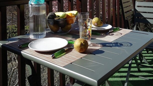 Une table dressée à l’extérieur, avec une vue sur la montagne, un saladier rempli de fruits, une bouteille d’eau et un verre.
