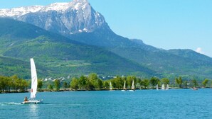 Un lac où voguent des voiliers, une montagne en arrière-plan et une rive bordée d’arbres et de bâtiments.