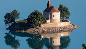Une petite île avec un seul bâtiment, entourée d’une eau calme et d’arbres.