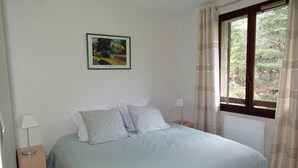 Une chambre à coucher avec un lit, deux tables de chevet, une fenêtre avec des rideaux et un tableau au mur.